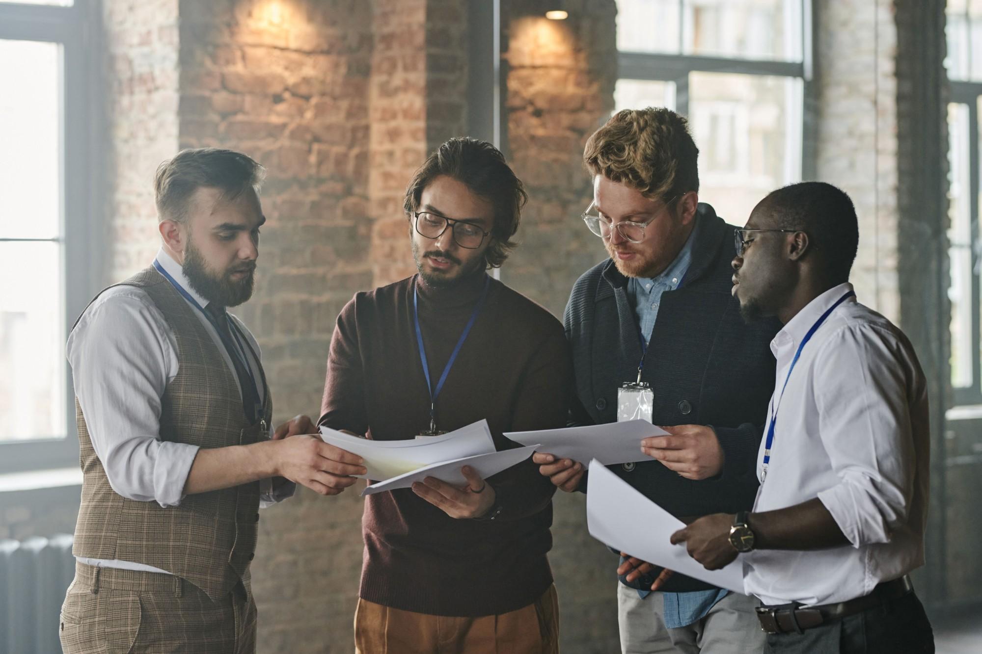 Four colleagues standing together comparing printed documents